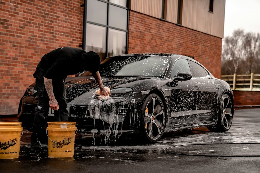 Detailer hand-washing a black sports car with foam