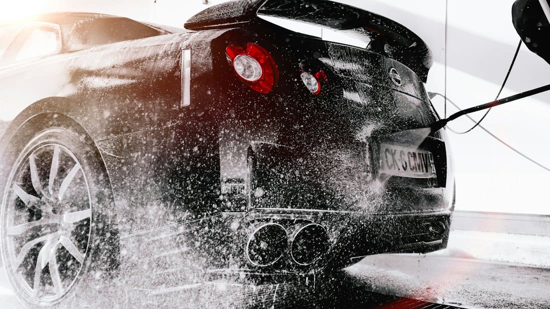 Pressure washer rinsing the rear of a black sports car