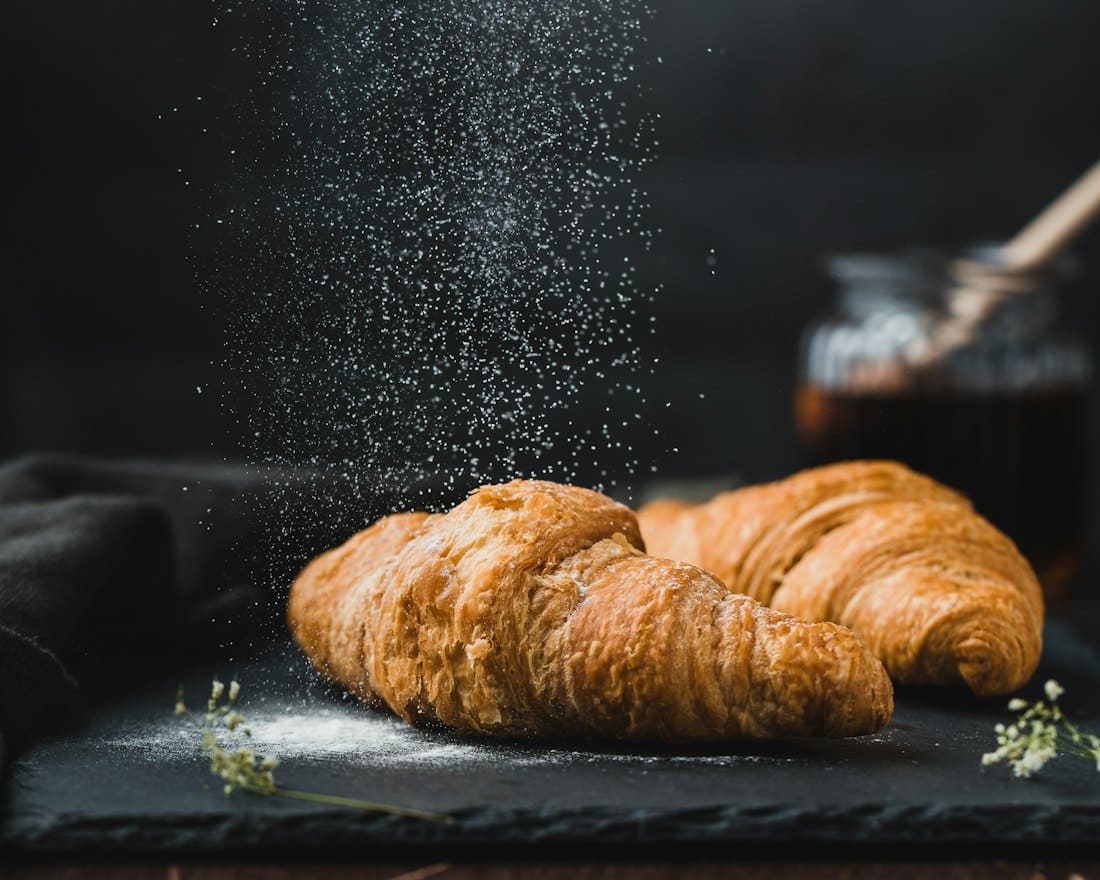 Two golden croissants on slate with a dusting of sugar