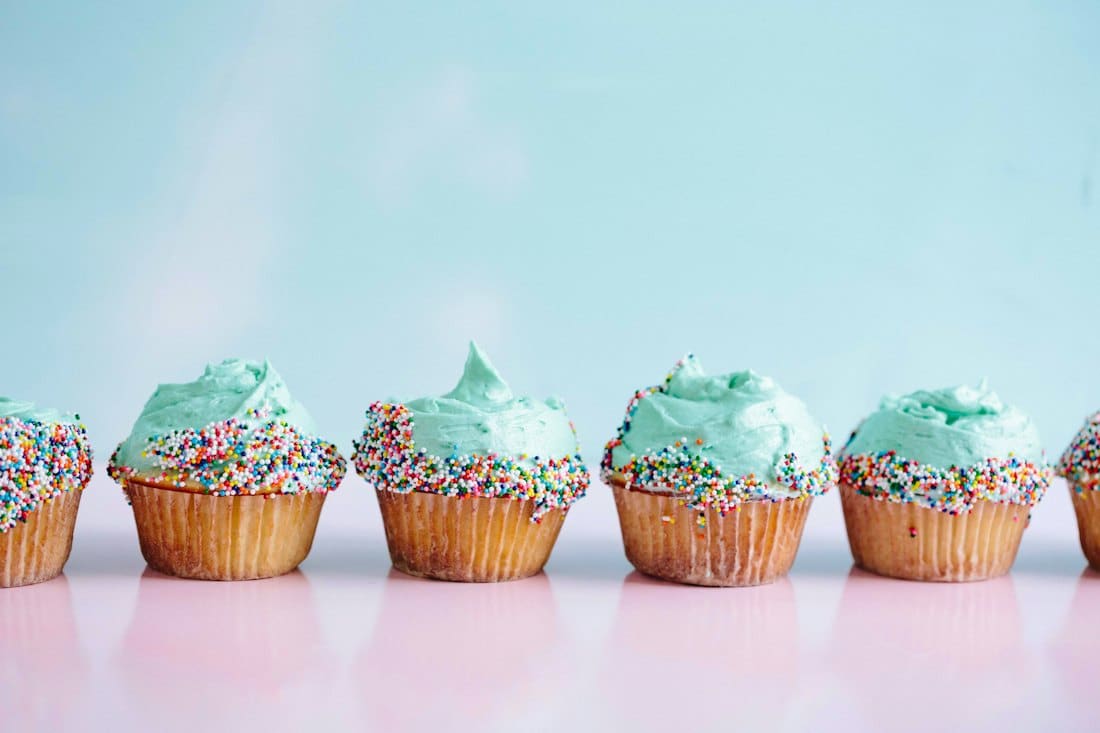 A row of cupcakes with mint frosting and rainbow sprinkles