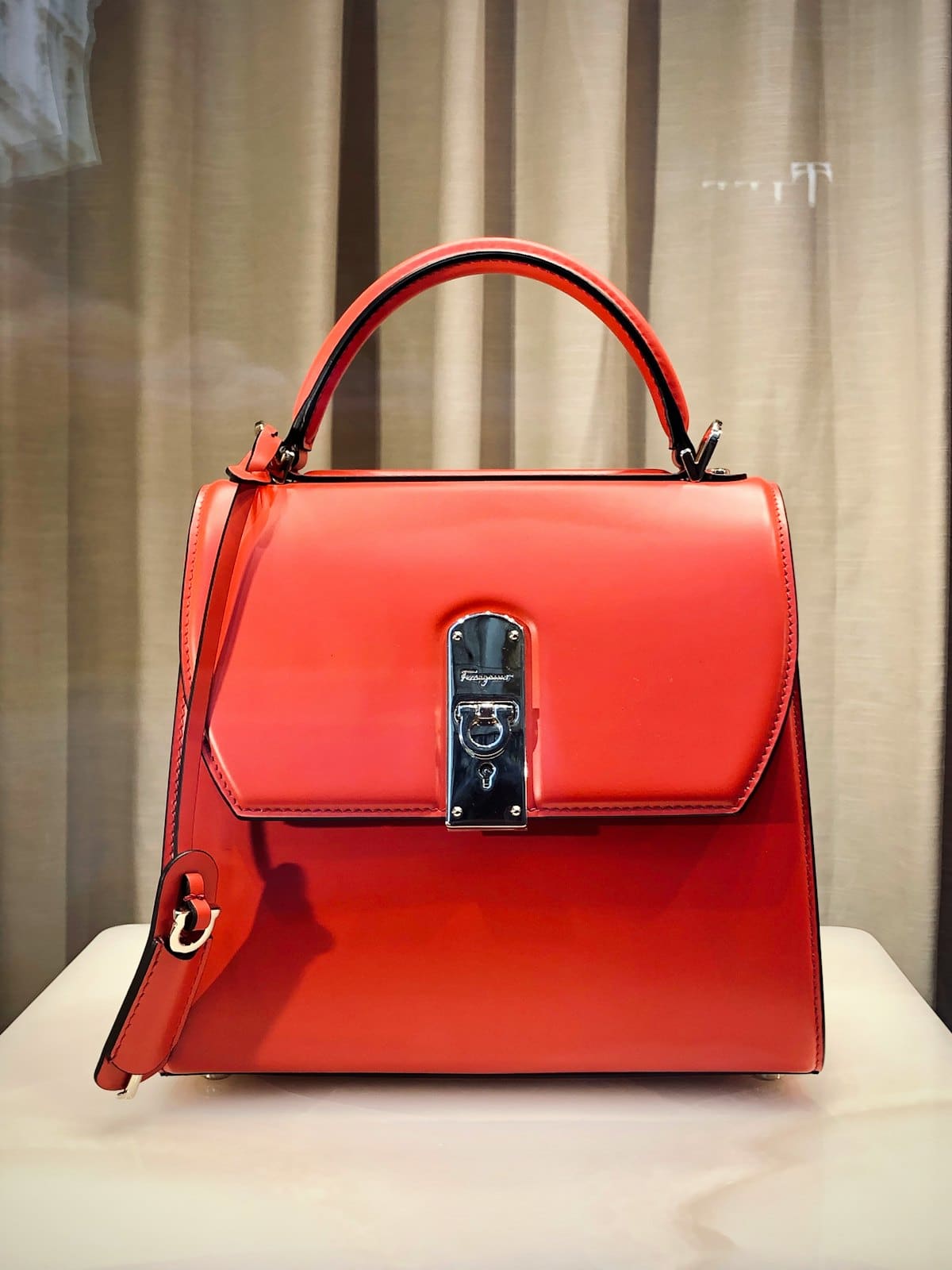 Structured red leather top-handle bag on a plinth
