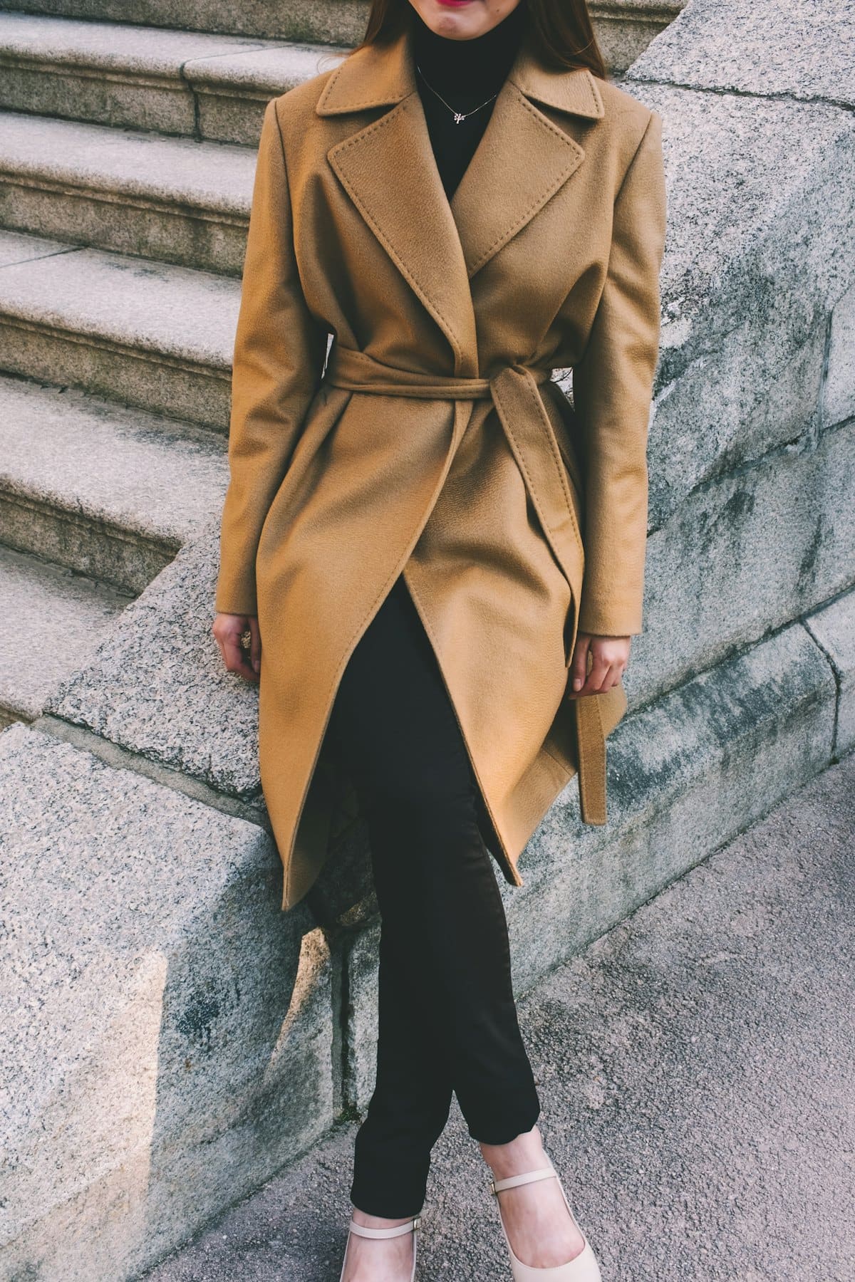 Woman on stone steps wearing a belted camel trench coat