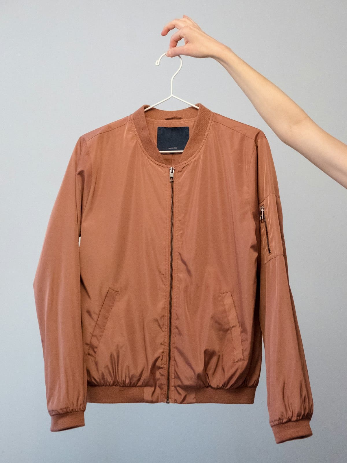 Terracotta satin bomber jacket held up on a hanger