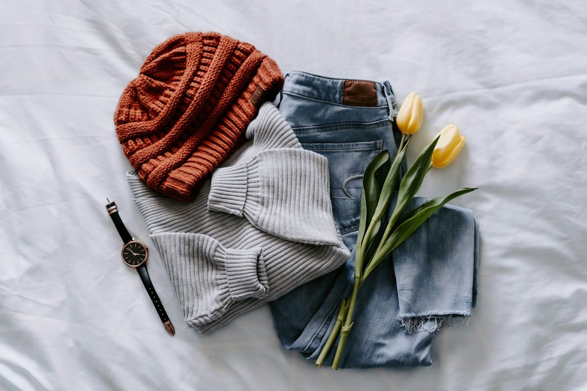 Flat lay of a grey knit jumper, rust beanie and denim
