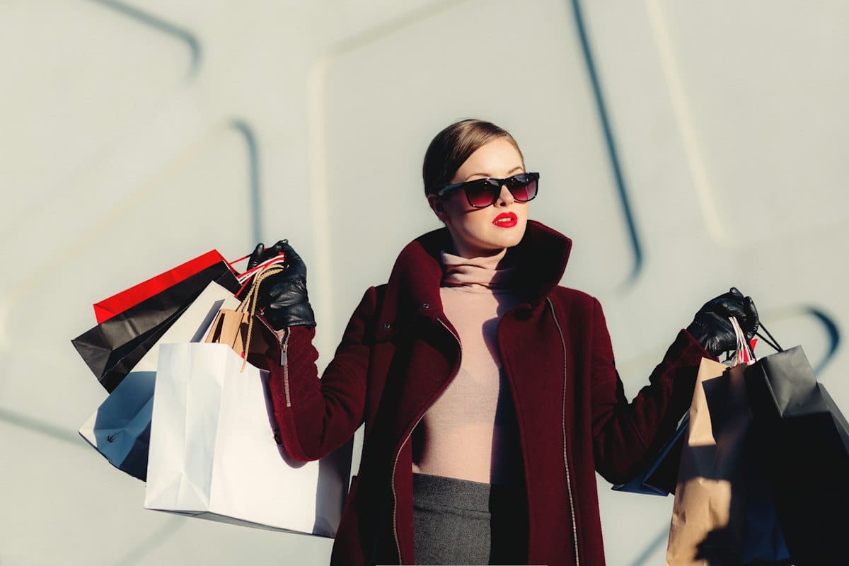 Woman in a burgundy coat and sunglasses carrying shopping bags