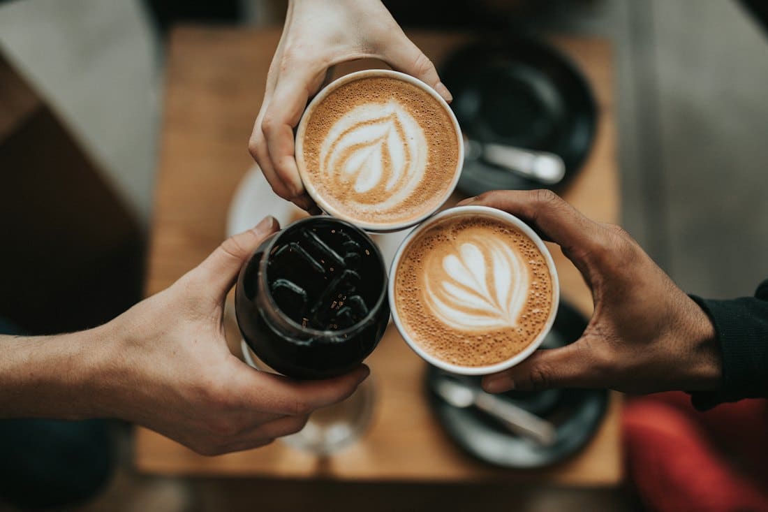 Friends toasting with two latte art cappuccinos over a table