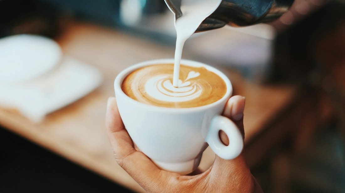 Barista pouring steamed milk into a latte to form a rosetta