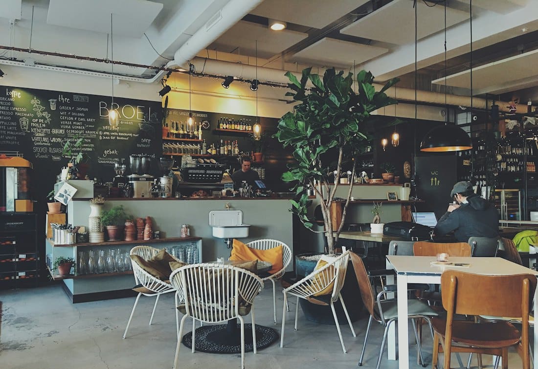 Busy café floor with rattan chairs, plants and a chalkboard wall
