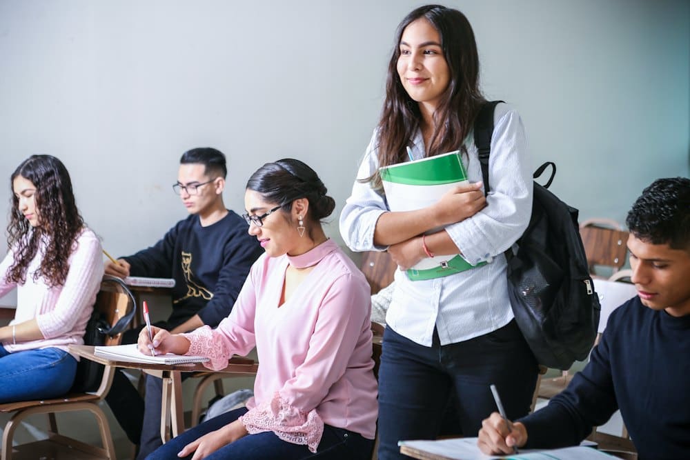 Secondary students working at desks while a classmate holds her books