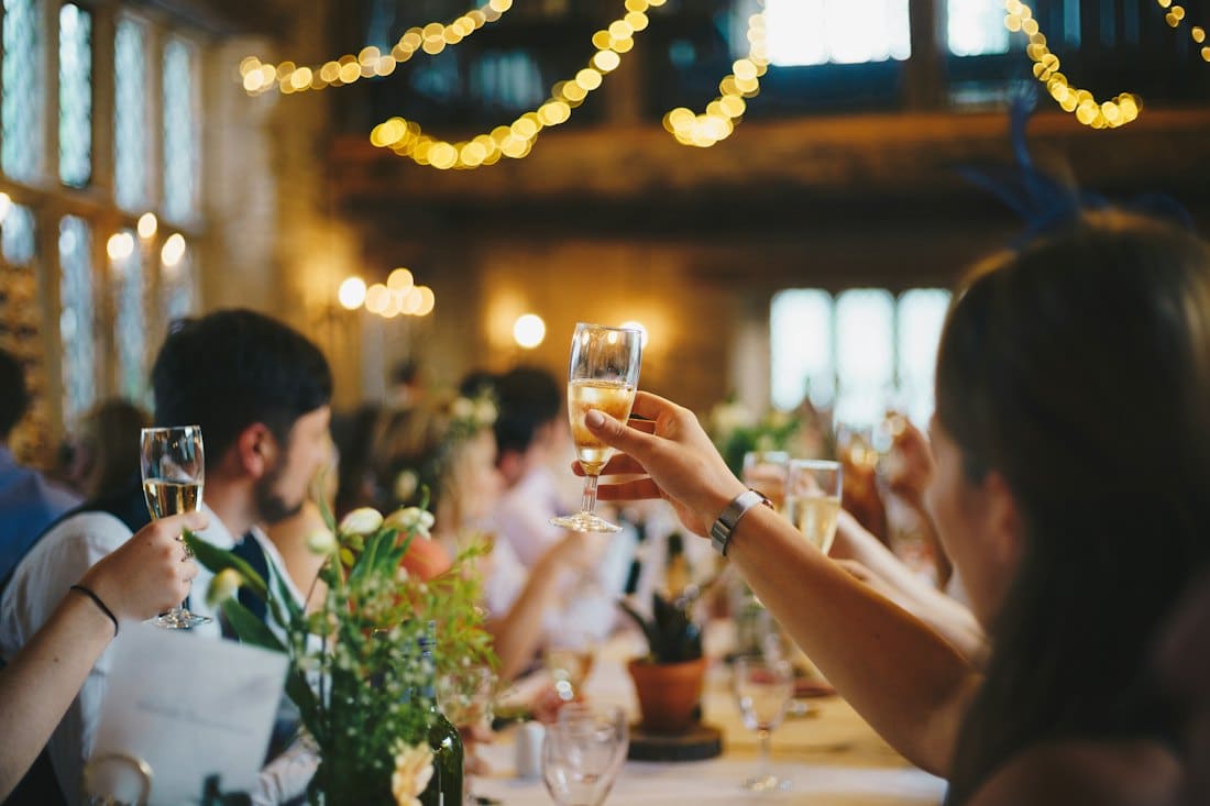 Guests raising champagne glasses at a candlelit table under fairy lights
