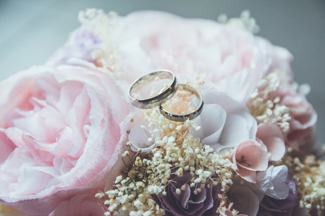 Two gold rings resting on a bouquet of blush peonies and baby’s breath