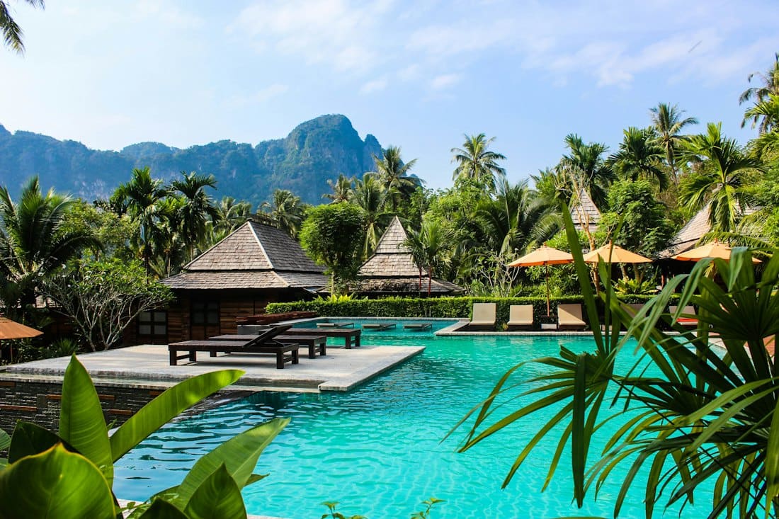 Thatched villas around a turquoise pool beneath green mountains