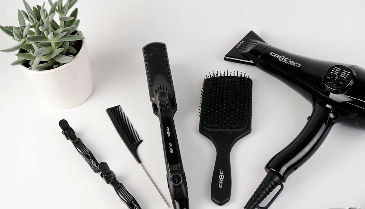 Professional hairdryer, brushes and styling tools laid out on white