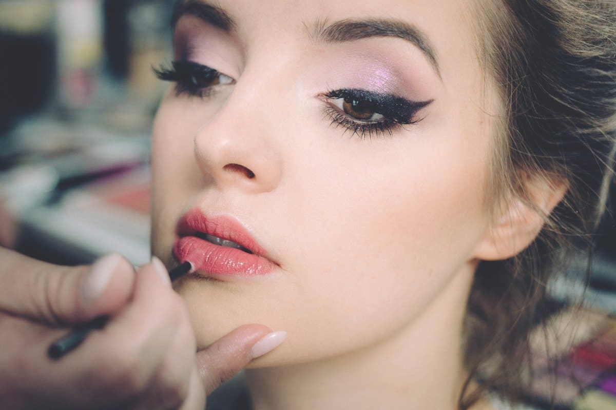 Makeup artist applying rose lipstick with winged eyeliner look