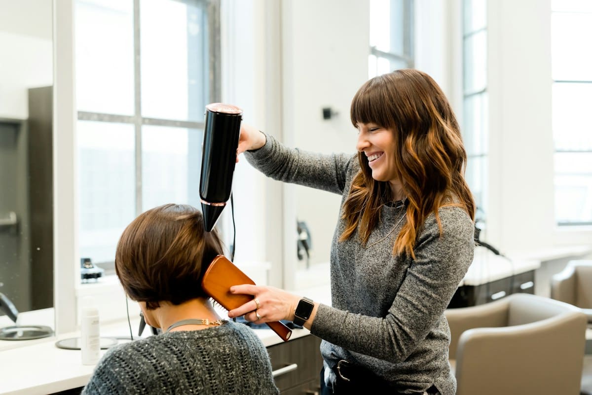Stylist shaping a short bob with a hairdryer in a bright salon