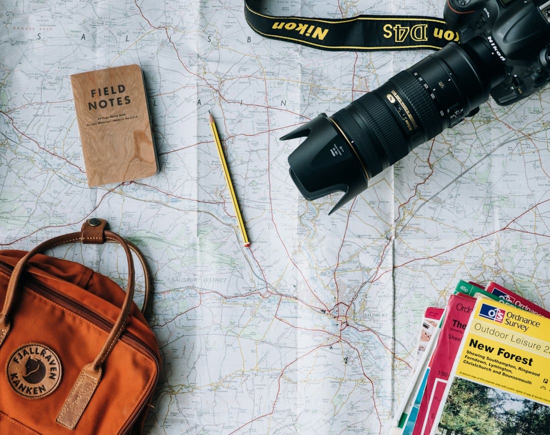 Map, camera, notebook and backpack laid out for trip planning